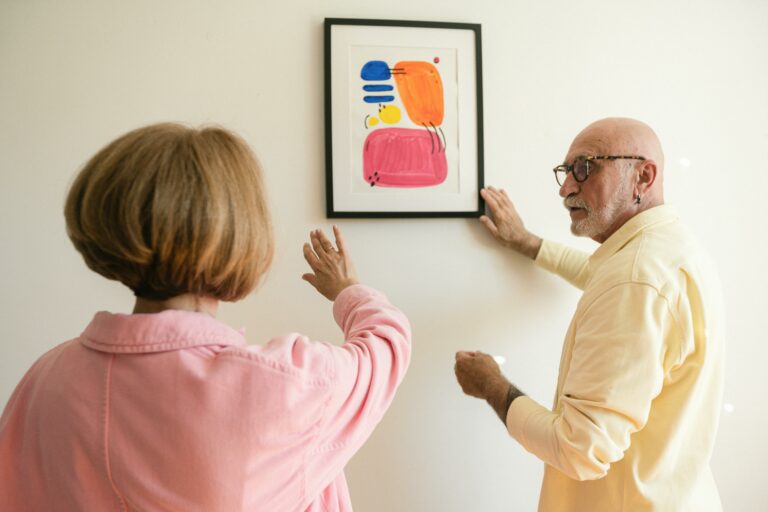 Senior couple hanging colorful modern artwork, showcasing their artistic taste.